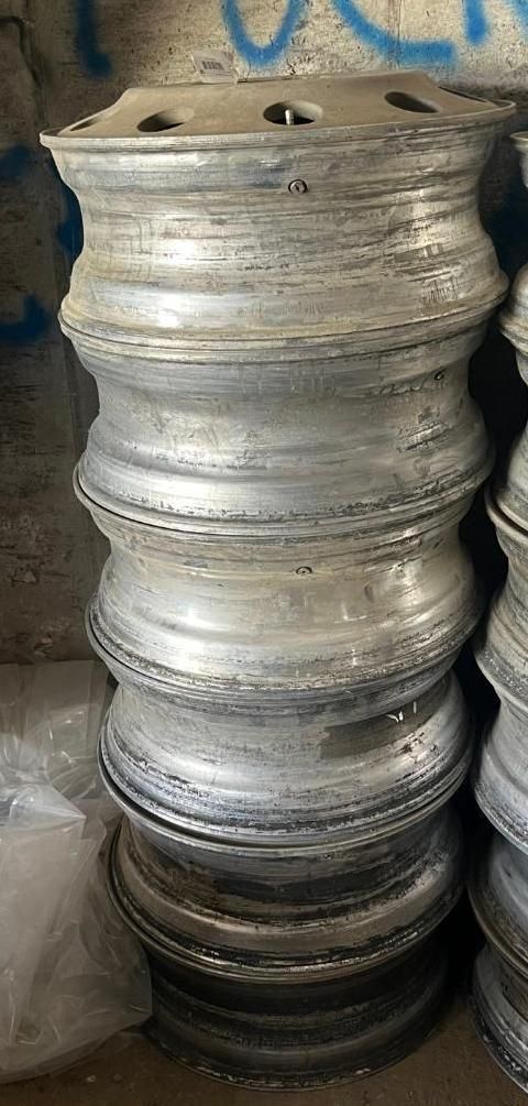 Stack of silver-colored, vehicle rims, in an indoor setting.
