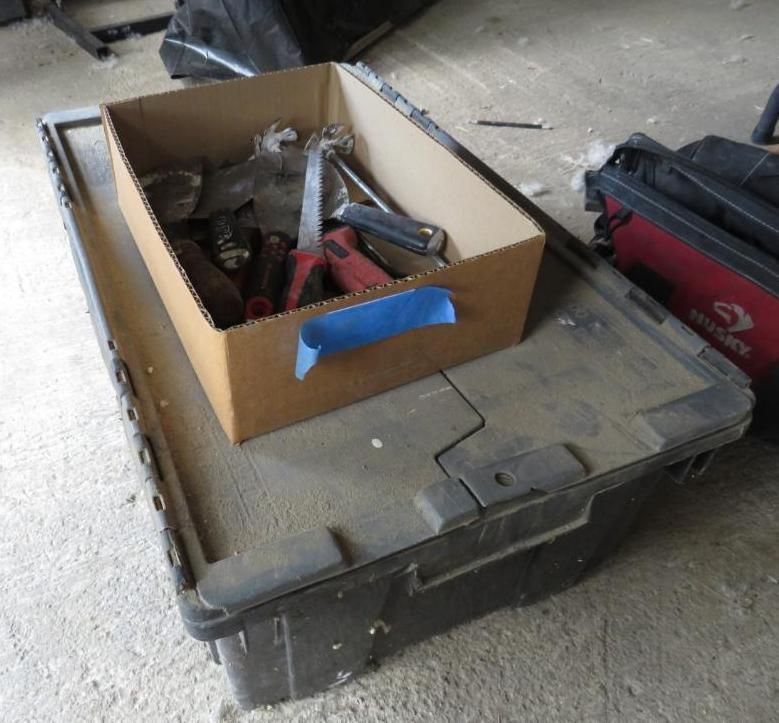 Cardboard box of tools on top of a dark gray storage container, with a red tool bag to the right.