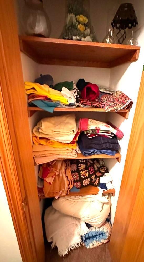 Wooden shelves in a closet, holding folded fabrics and decorative objects.