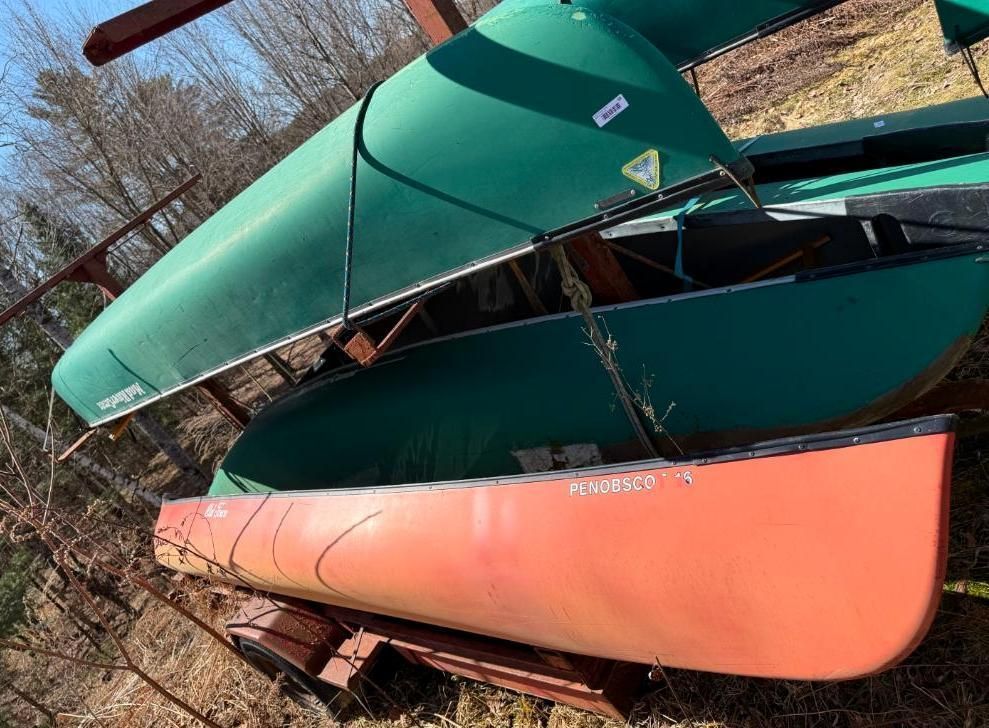 Three canoes stacked; red and two green. Outdoors, on a metal rack.