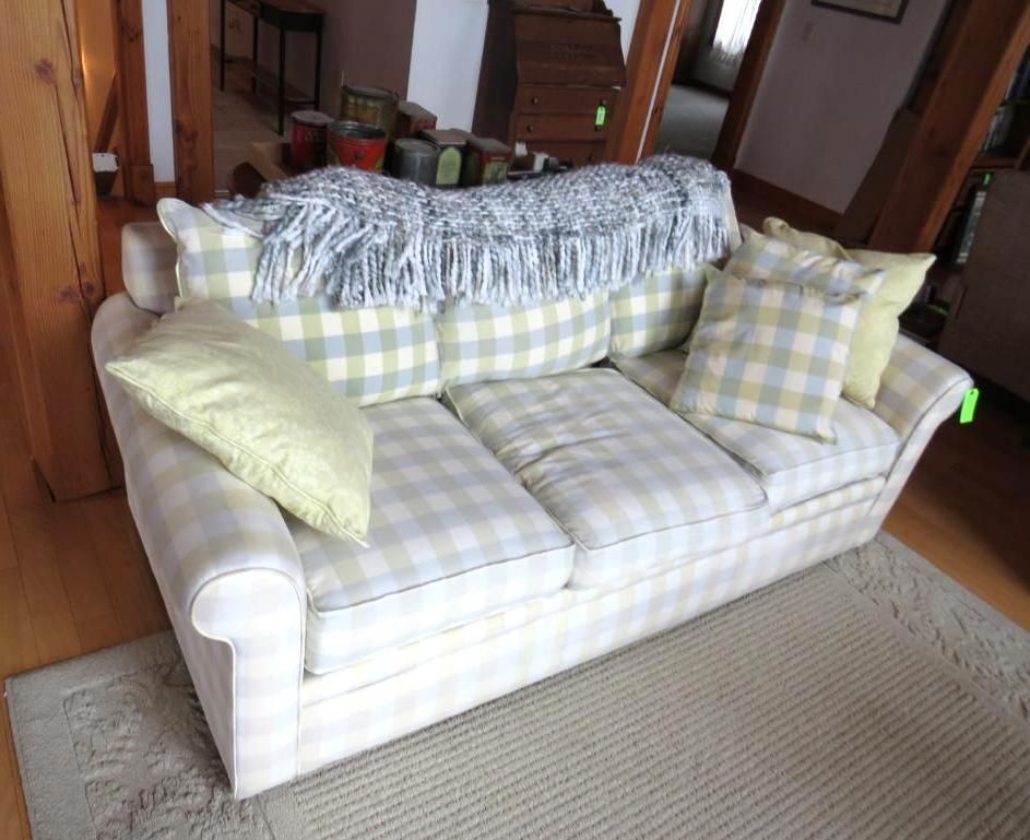Couch with light green checkered cushions and pillows, topped with a blue blanket.