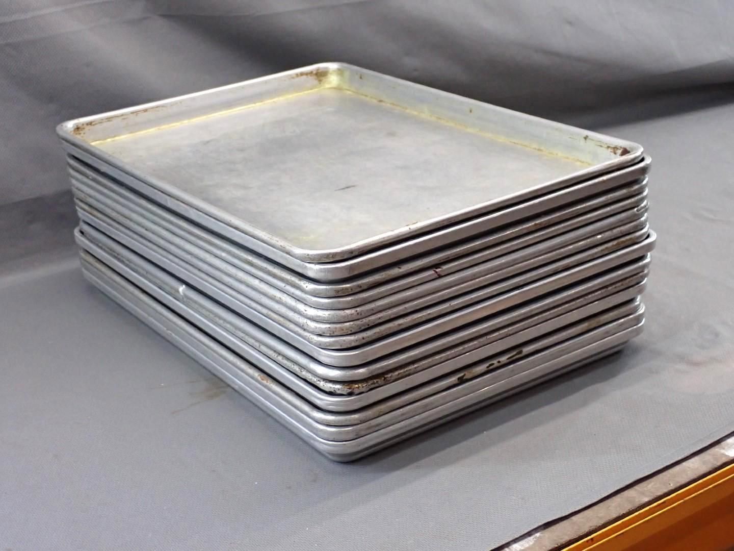 Stack of rectangular, metal baking sheets on a gray surface.