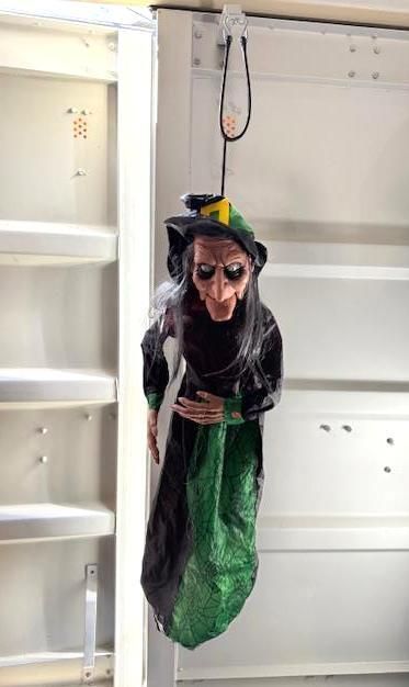 Hanging Halloween witch decoration with a green and black dress, black hat, and long nose.