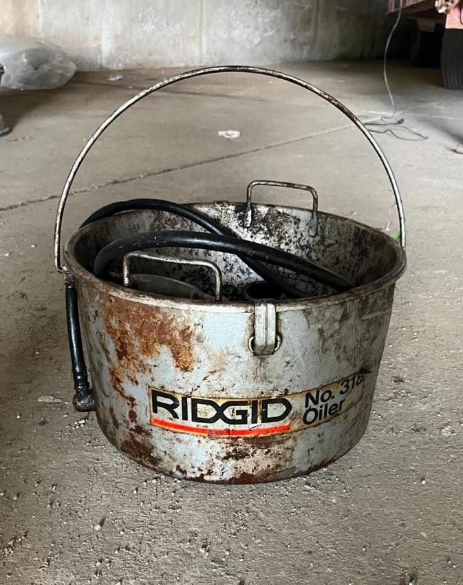 RIDGID No. 310 Oiler bucket with a handle, containing a black hose, sitting on a concrete floor.