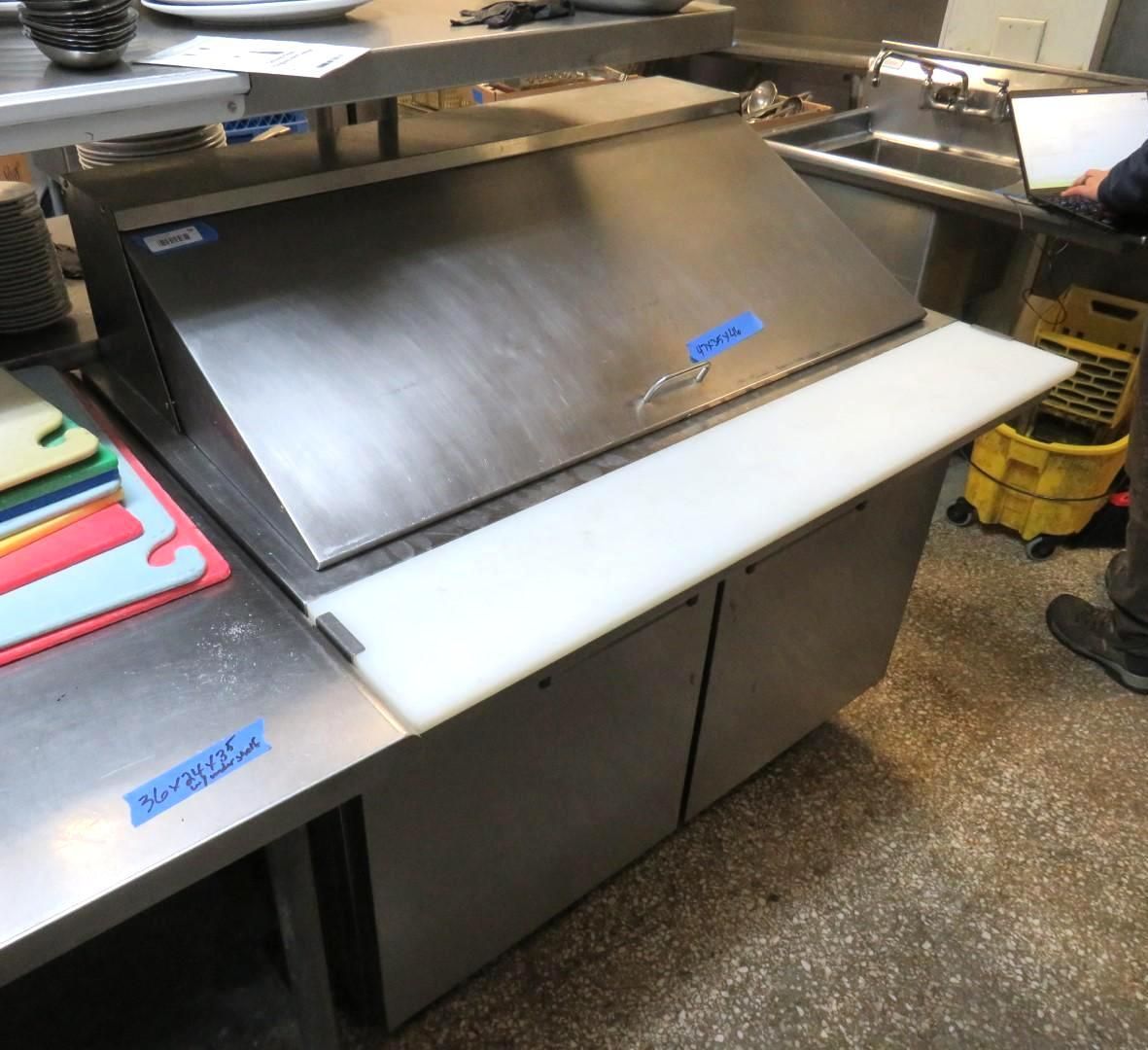 Stainless steel food prep station in a commercial kitchen with cutting boards and storage cabinets.