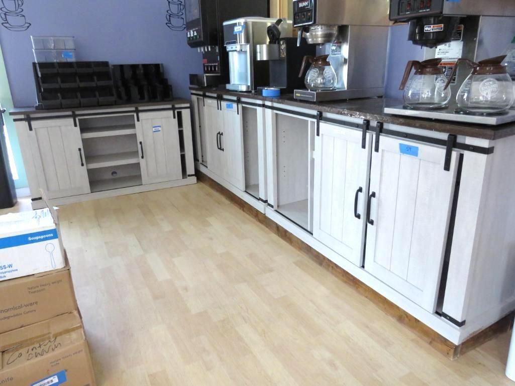 Coffee station with white cabinets, black hardware, coffee machines, and light wood flooring.