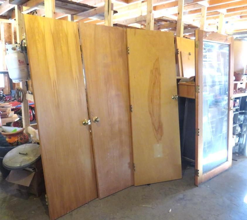 Four wooden doors leaning in a garage, one with a glass panel.
