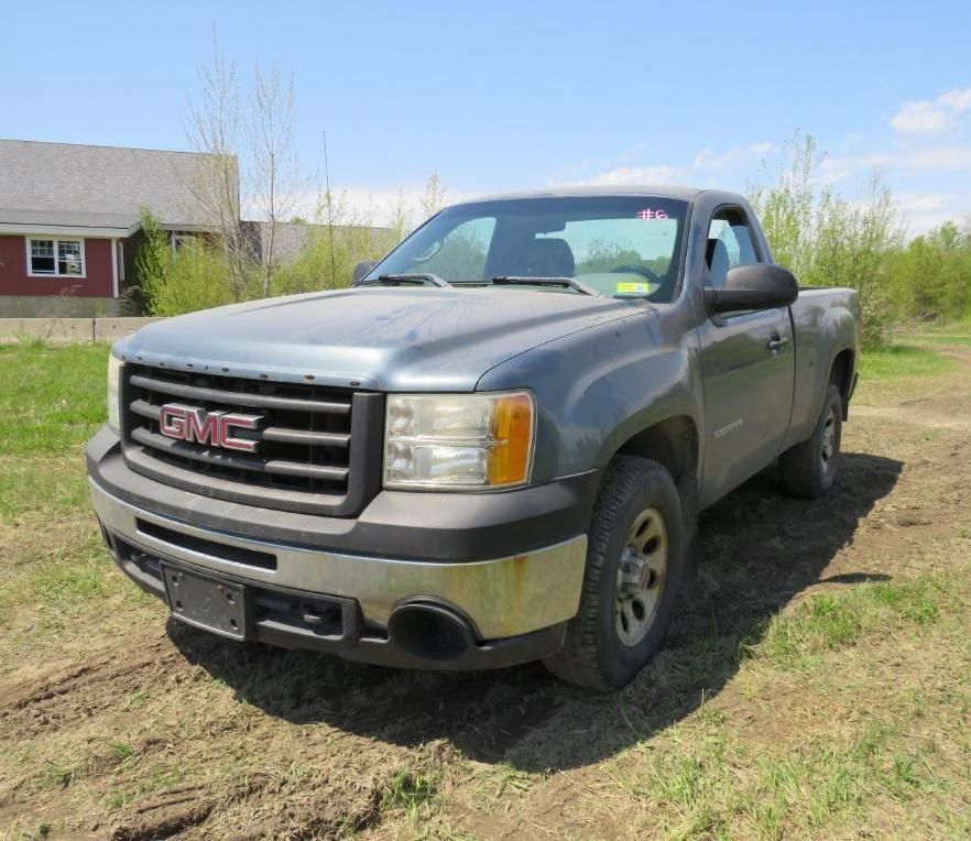 A gray GMC pickup truck parked on grassy ground, with a house in the background.