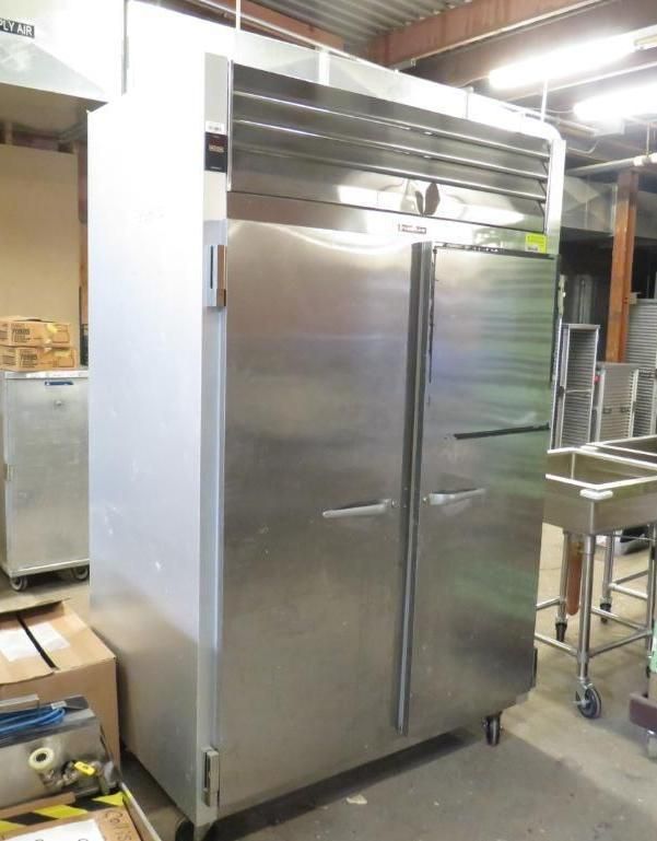 Large stainless steel commercial refrigerator with two doors, inside a warehouse.