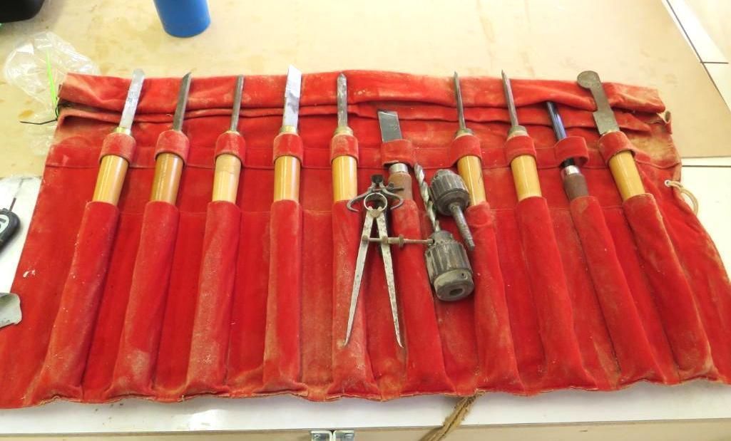 Red tool roll holding chisels, compass, a hammer, and other hand tools on a light surface.