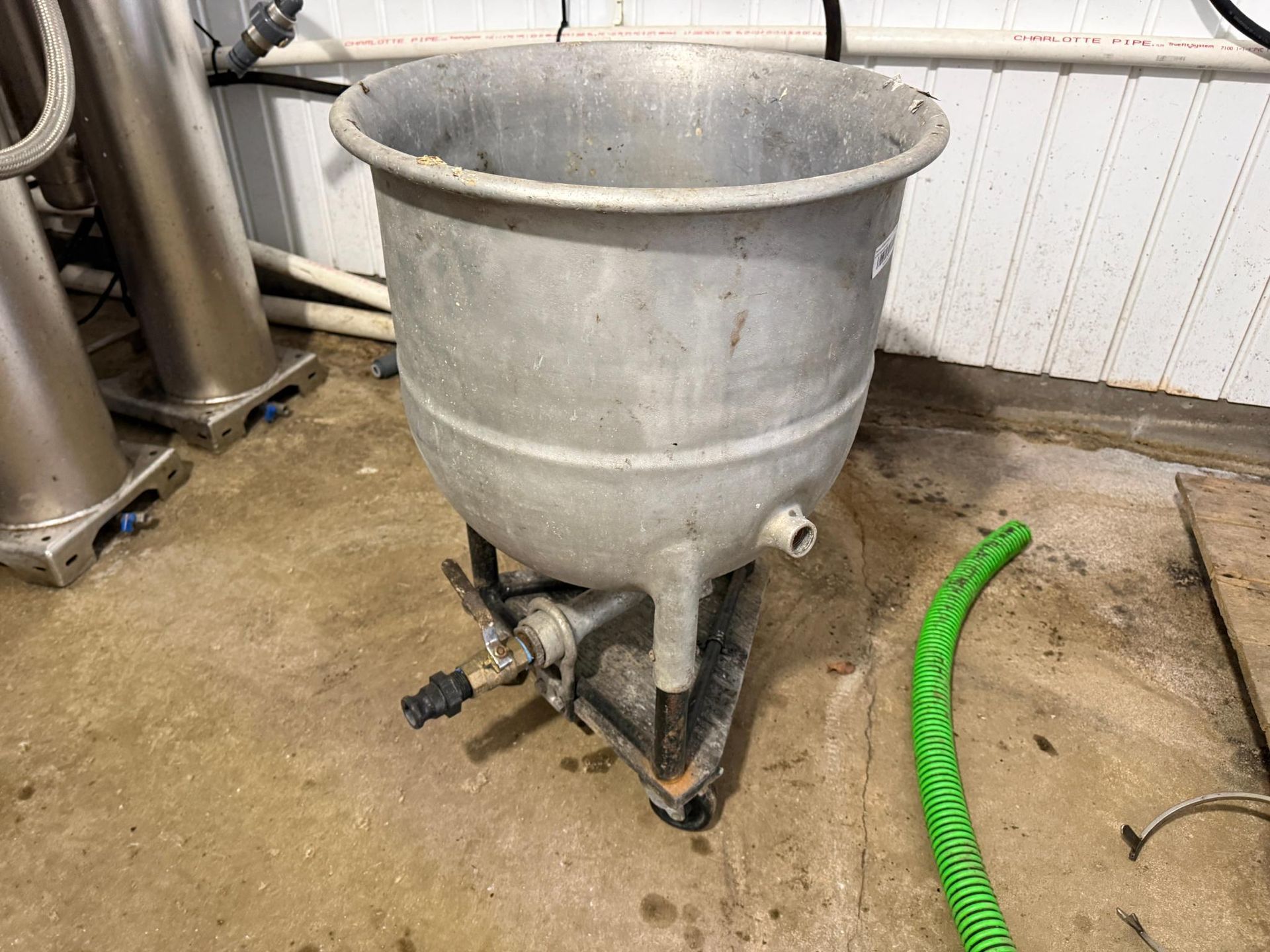 Large metal industrial vat on a wheeled stand, with a green hose nearby.
