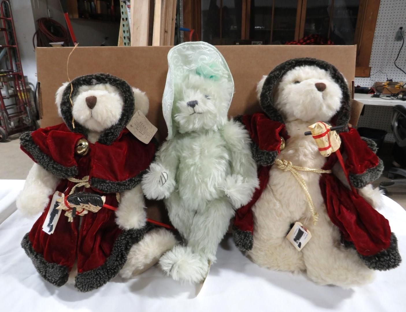 Three teddy bears: cream-colored with red capes and a green bear with a translucent hat.
