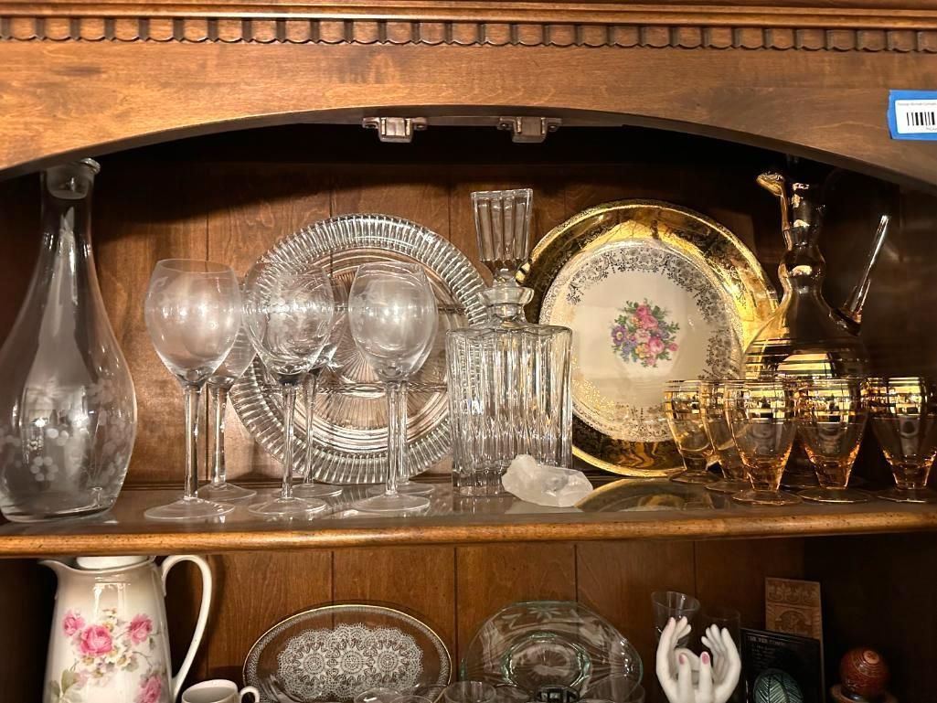 Wooden hutch with shelves holding glassware: decanters, plates, and glasses.