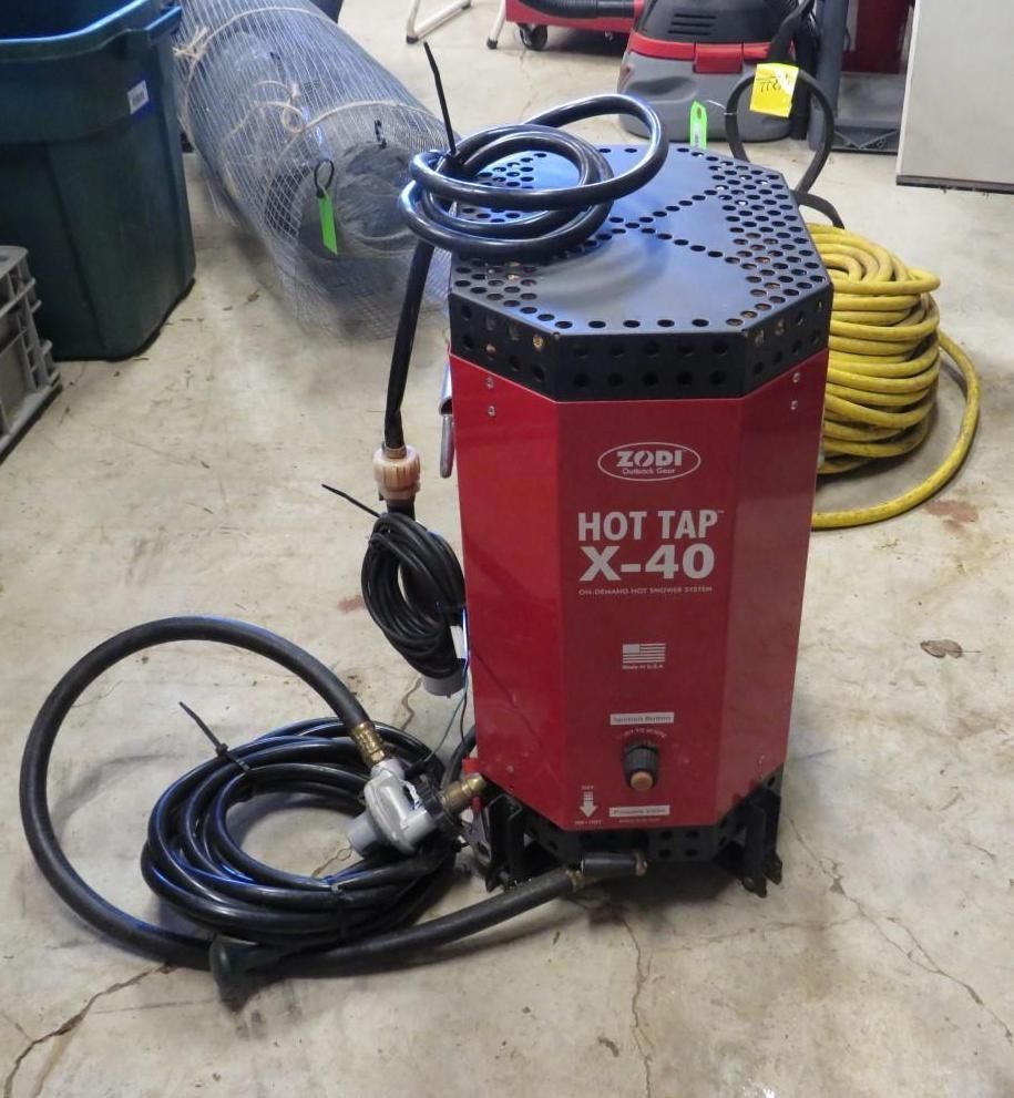 Red and black Zodi Hot Tap X-40 water heater on a concrete floor with hoses and a yellow extension cord.