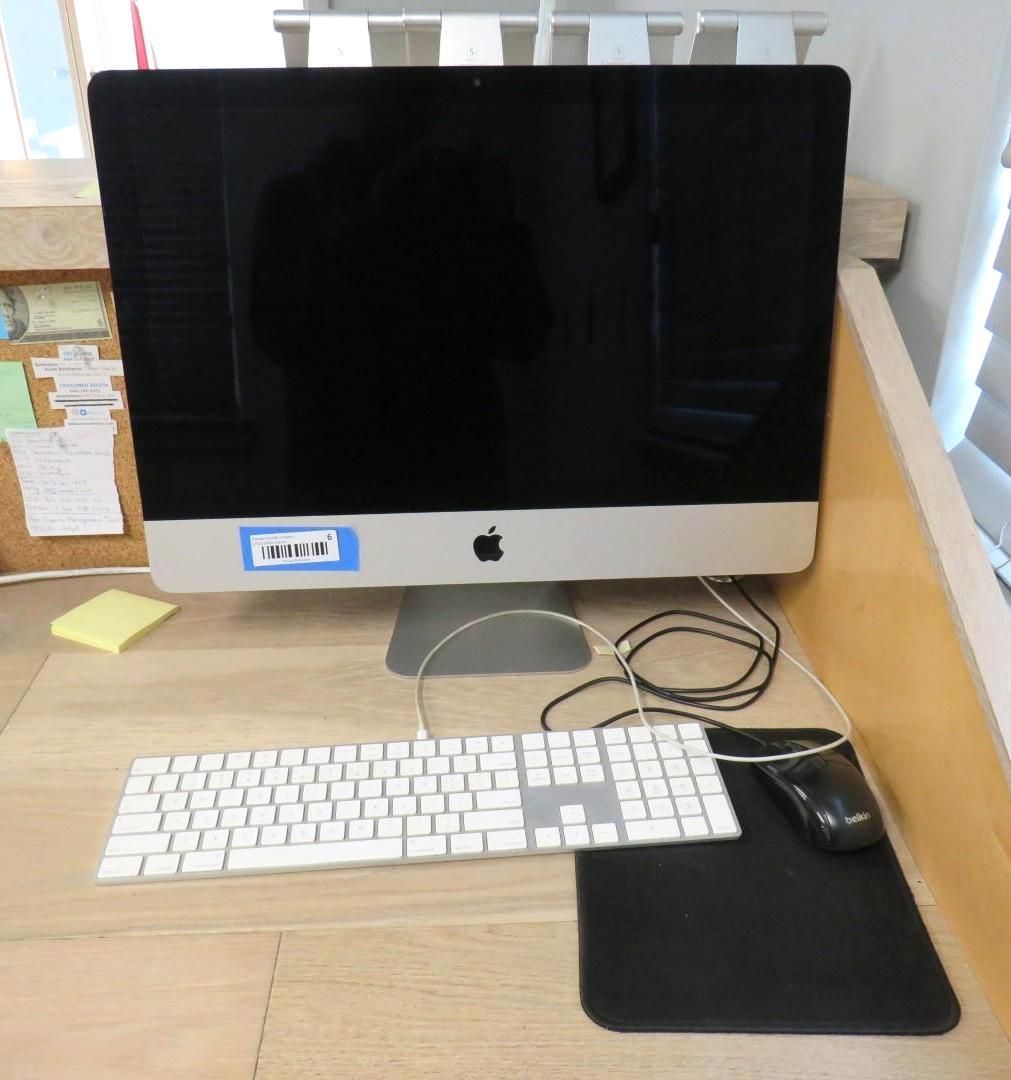 An iMac computer with a white keyboard and black mouse on a wooden desk.
