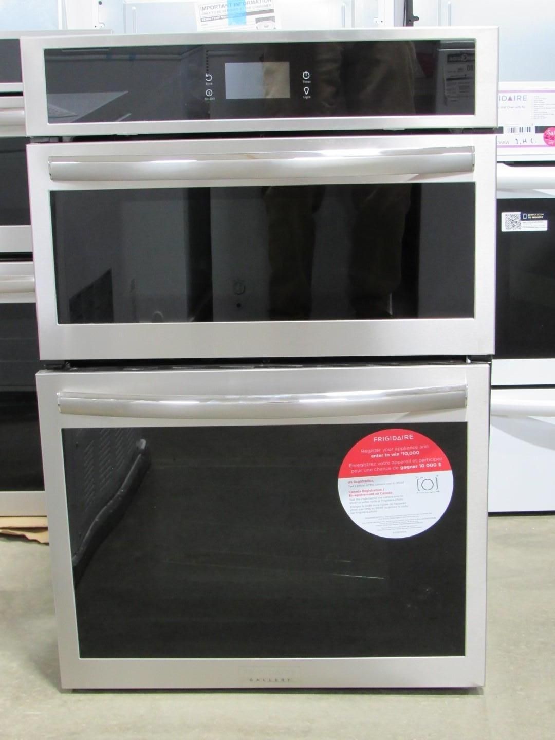 Stainless steel double oven appliance with black glass doors, in a store setting.