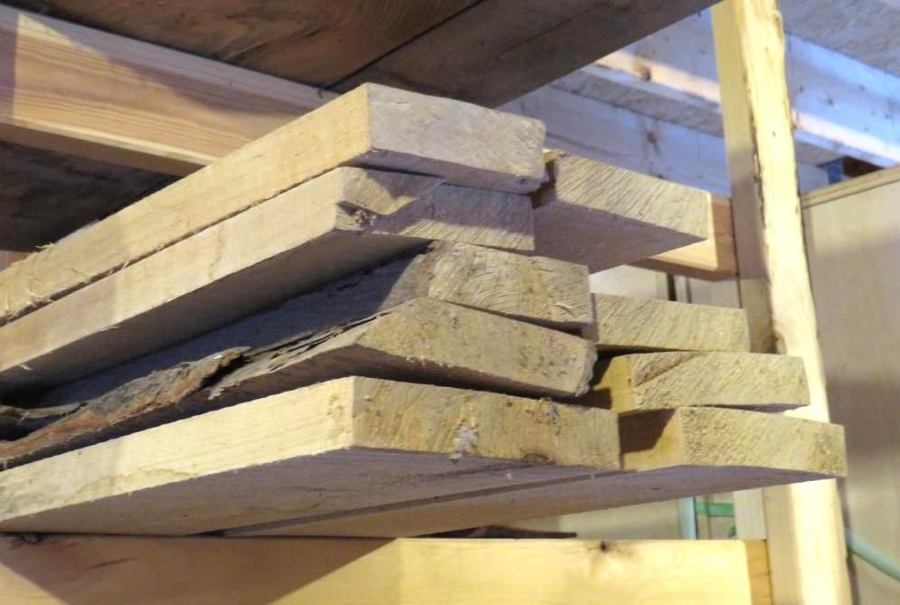 Wooden planks stacked on a wooden shelf in a storage space.