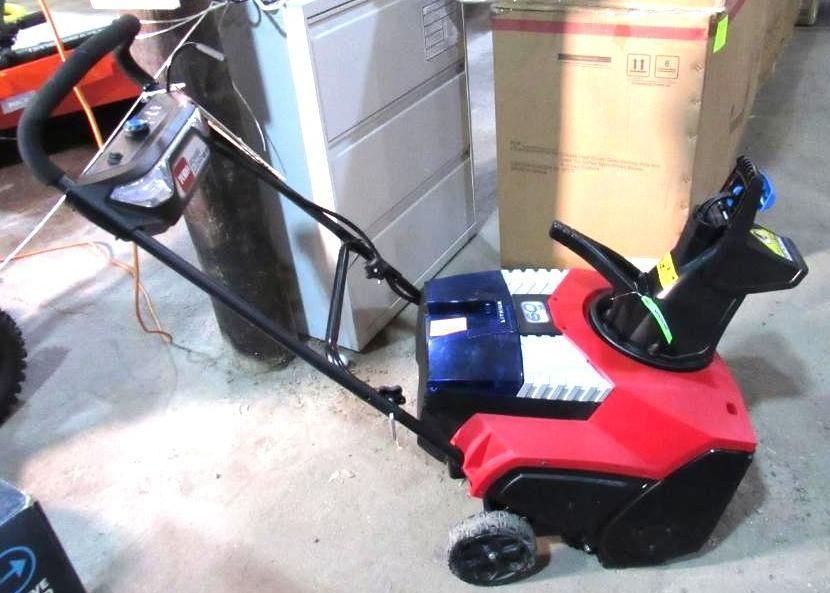 Red and black electric snowblower with blue accents, handles, and a control panel.  Standing on concrete.
