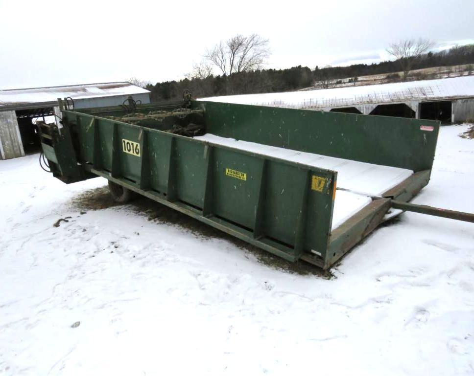 Green agricultural manure spreader in snow, outdoors.