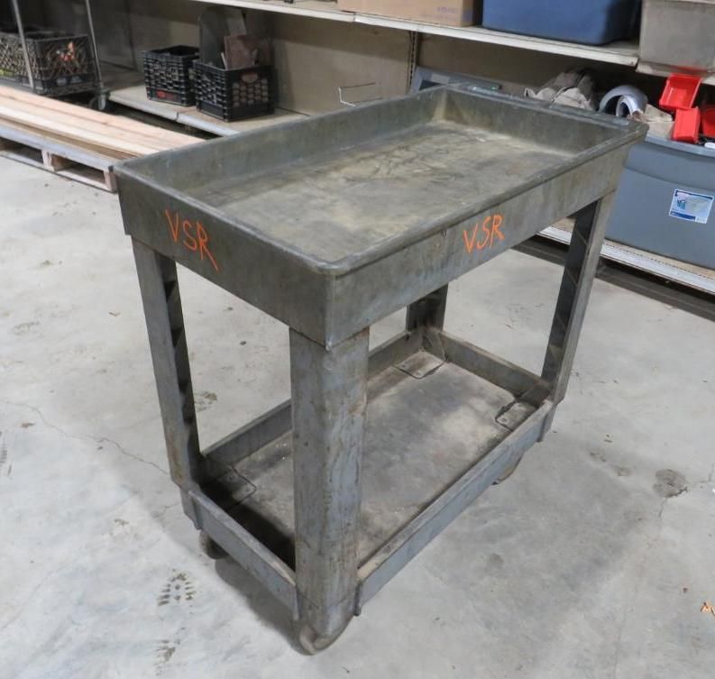 Gray metal utility cart with tray top and lower shelf; wheels on concrete floor.