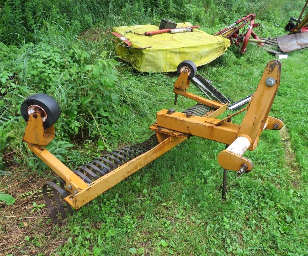 Yellow farm implement with rollers and spikes in a grassy field.