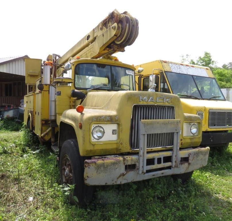 Yellow Mack truck with a boom lift parked outside, beside a yellow van.