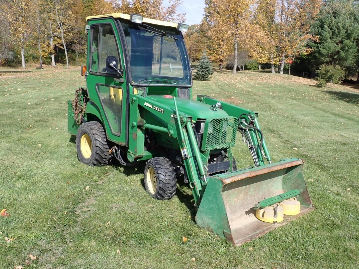 Green compact tractor with front loader on a grassy field in autumn