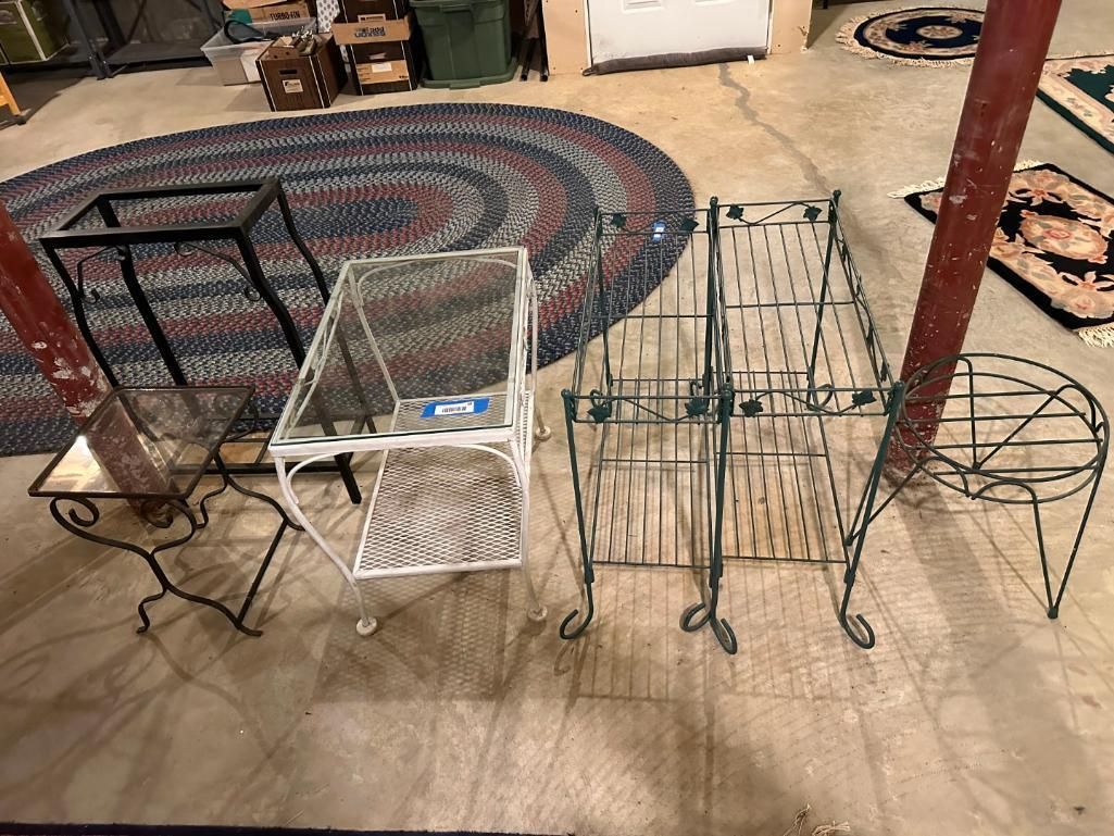 Metal plant stands and tables on a concrete floor near an oval rug.