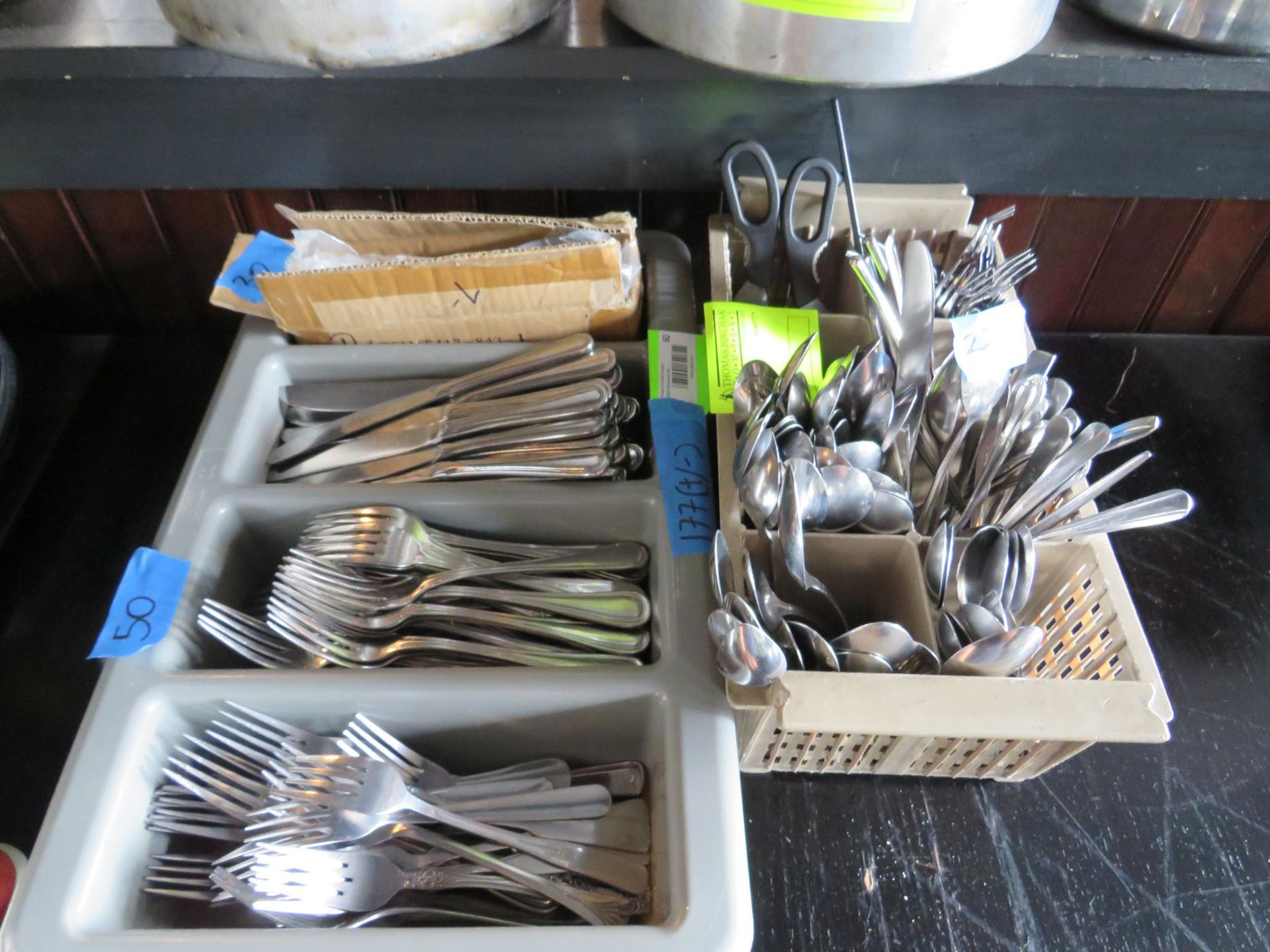 Utensils sorted in trays and basket; knives, spoons, forks, and scissors, possibly for a restaurant.