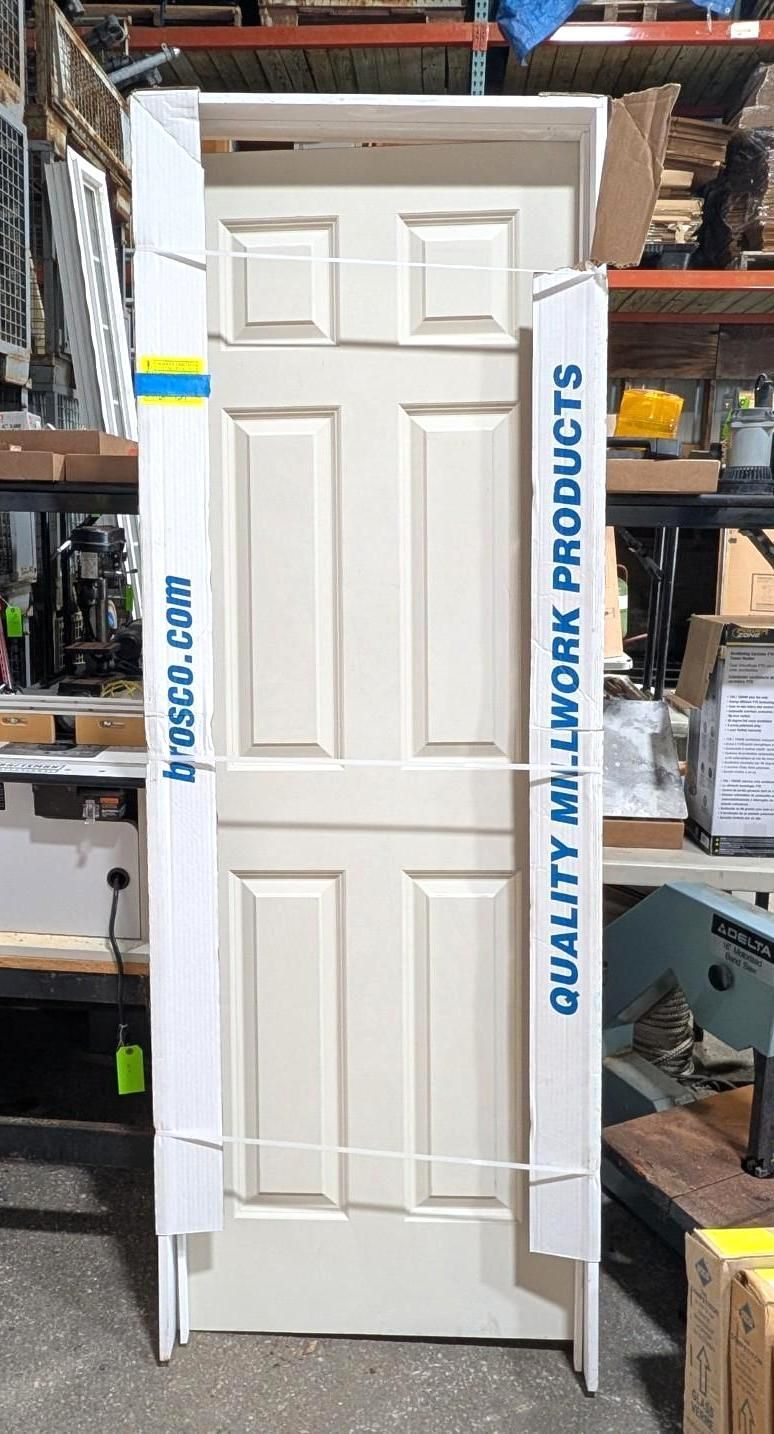 White interior door displayed in a warehouse, with “QUALITY ALL WORK PRODUCTS” on the stand