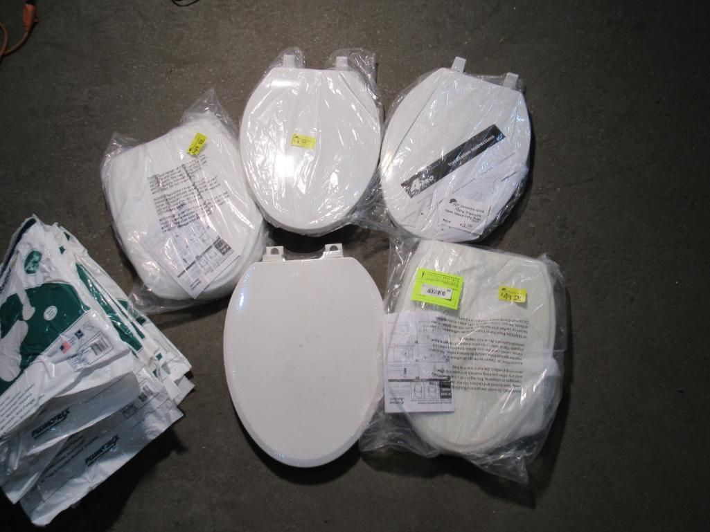 Several white toilet seats in plastic packaging on a dark surface.