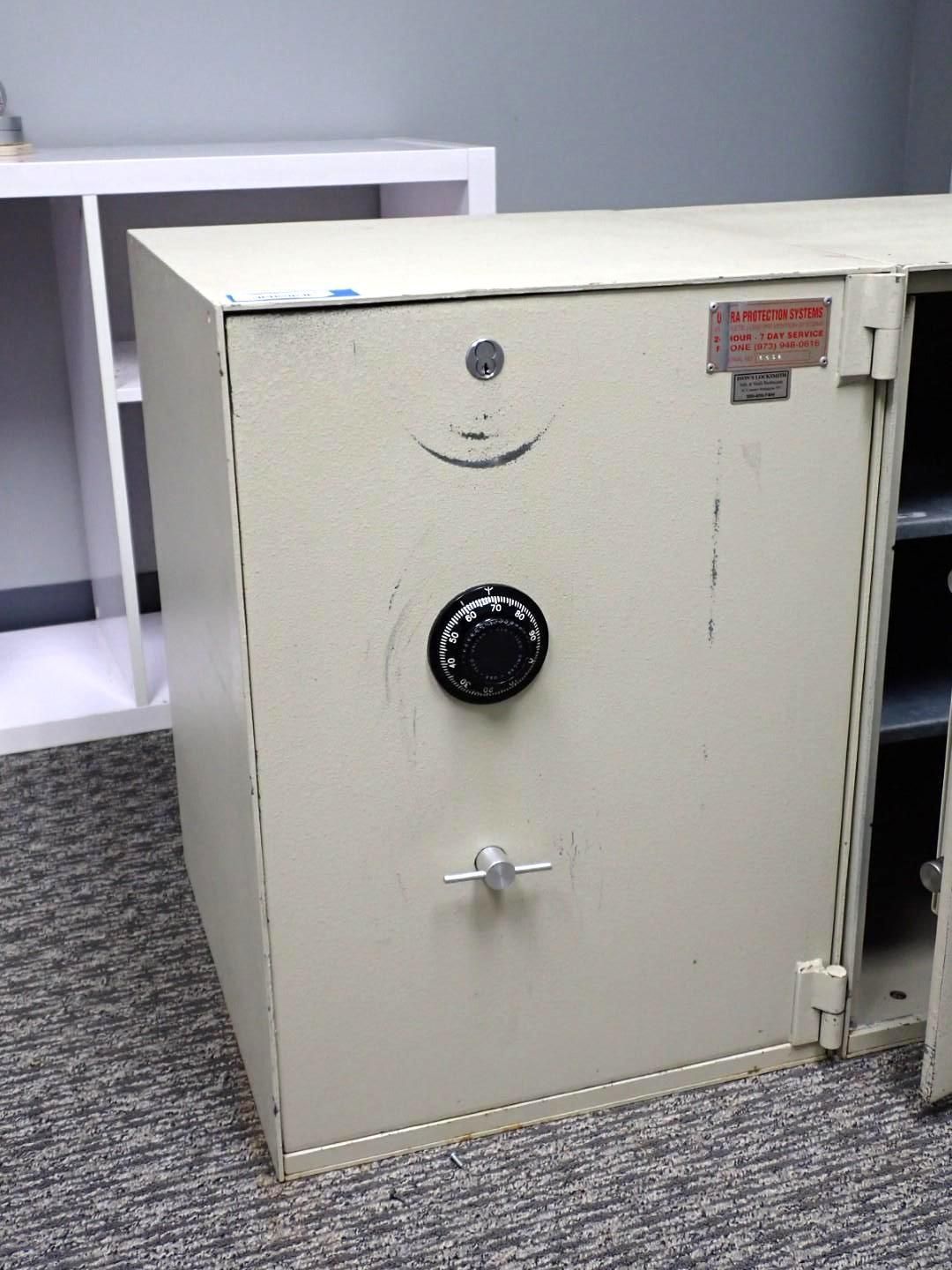 A beige metal safe with a combination dial, handle, and open door on a carpeted floor.