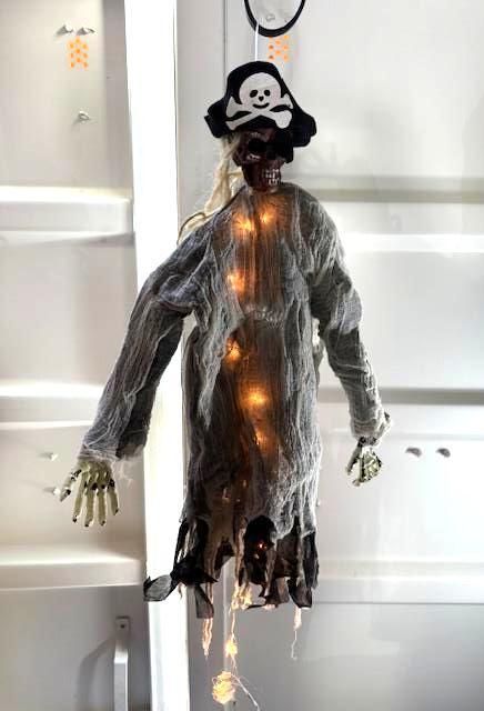 Halloween skeleton decoration wearing a pirate hat, lit up, hanging indoors.