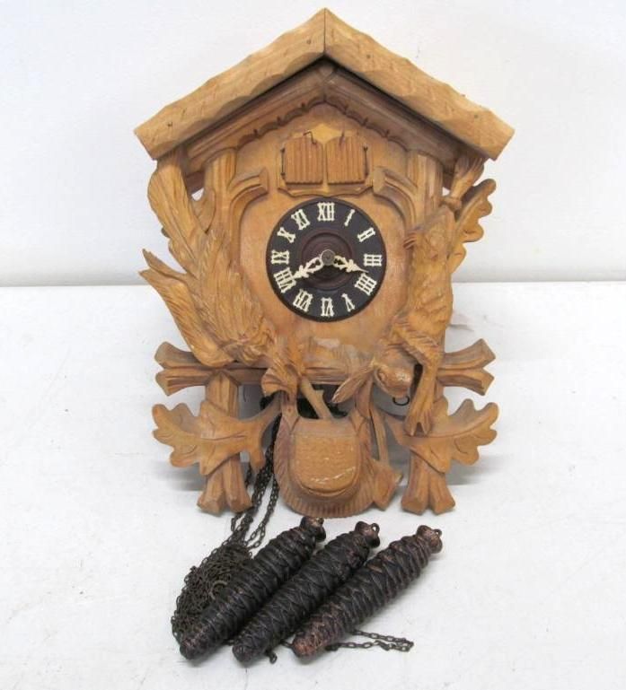 Wooden cuckoo clock with carved leaves, birds, and pinecone weights. Black clock face with Roman numerals.