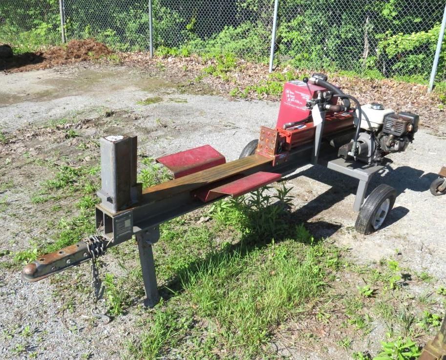 A red and gray gasoline-powered log splitter outdoors with a black motor and a steel beam.