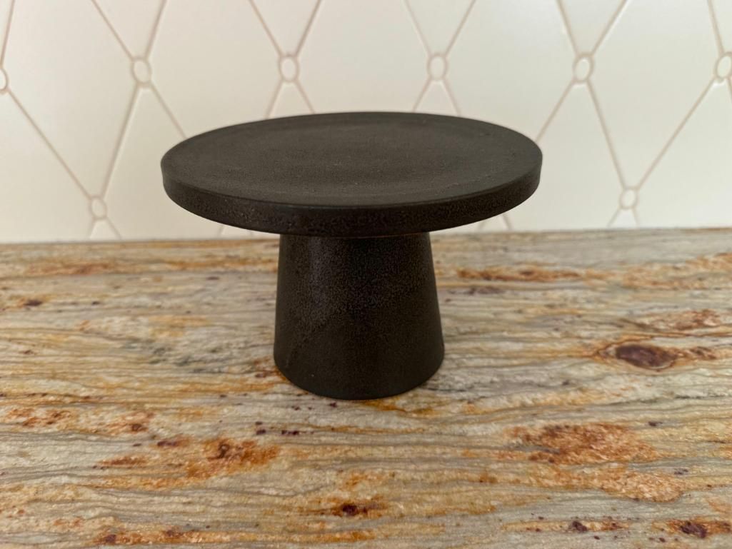 Small, black, pedestal-style table on a speckled, light-brown surface.