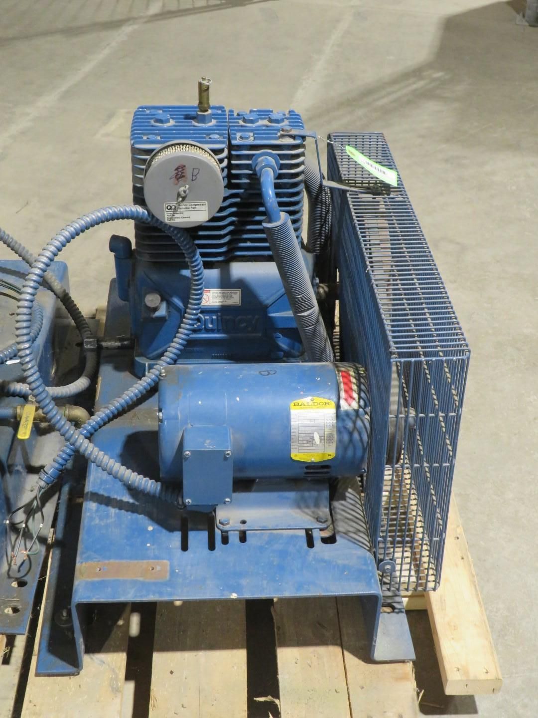 Blue industrial air compressor on a wooden pallet; has a protective wire cage.