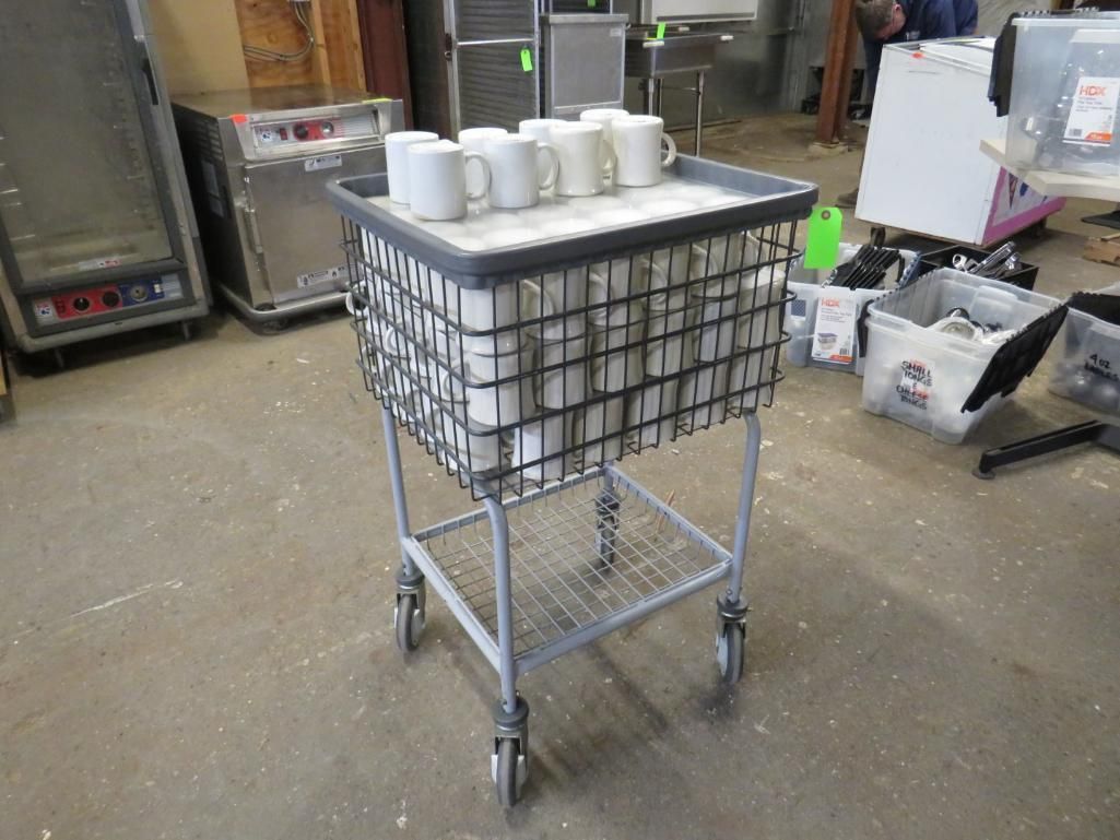 Gray cart holding white mugs and dishware. The cart is on a concrete floor in a warehouse.