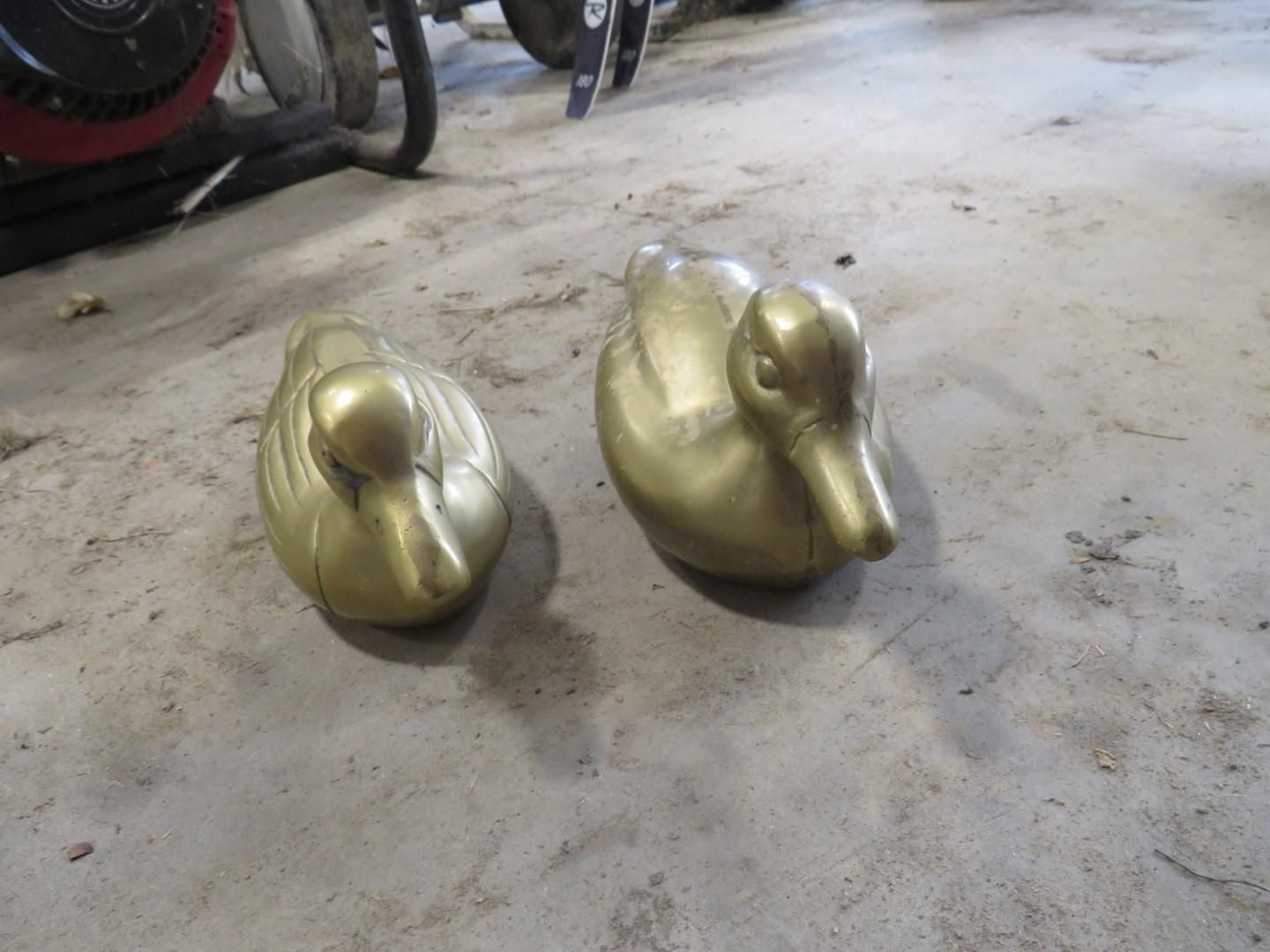 Two brass duck statues on a concrete surface.