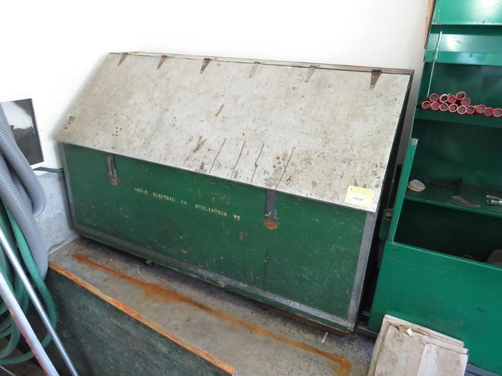 Green metal tool chest with a white lid, leaning against a green cabinet.