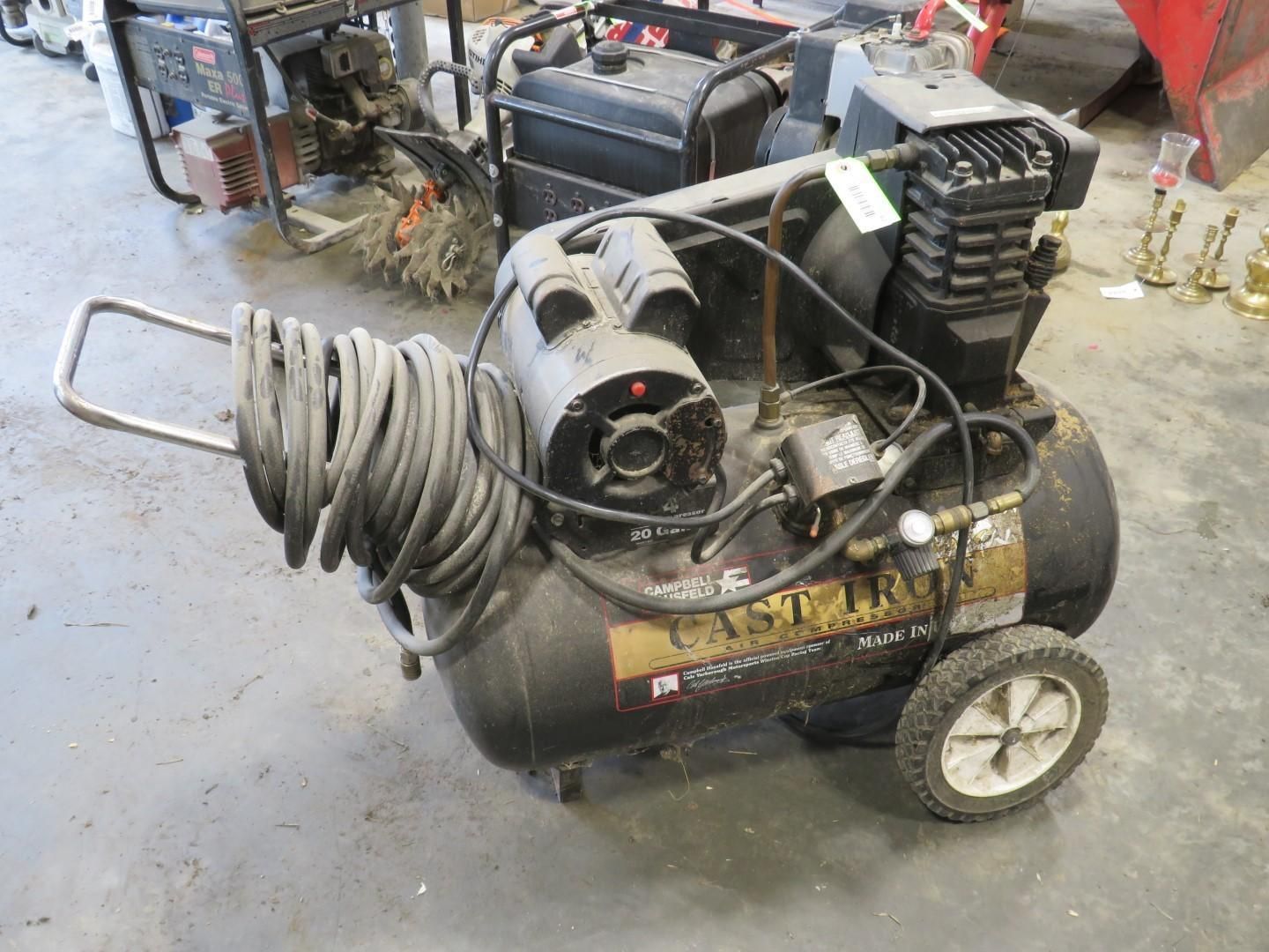Black air compressor with hose coiled on handle, on wheels, outside.