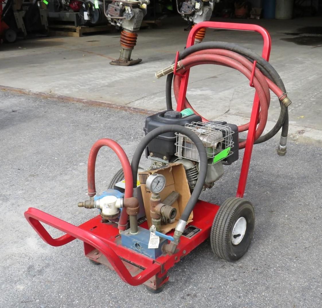Red wheeled pressure washer with engine and hoses, outdoors.