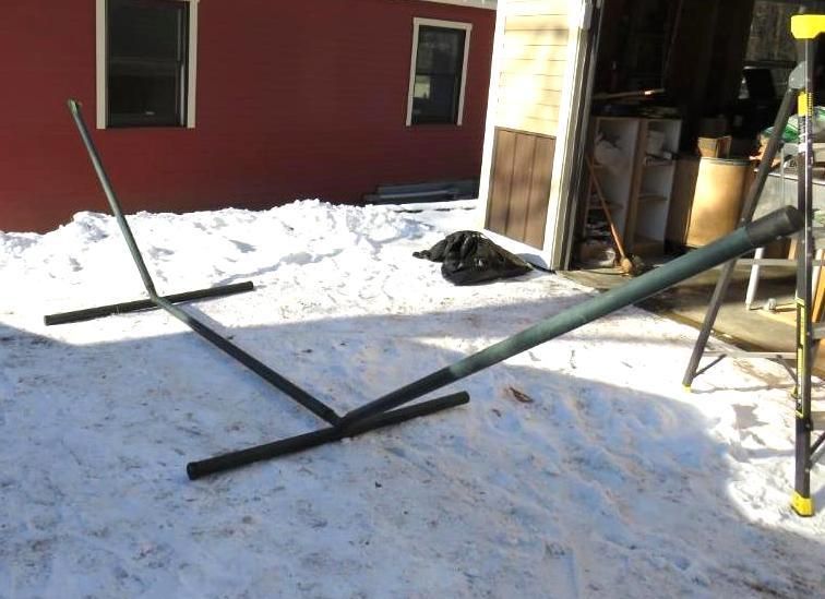 A metal hammock stand on snow in front of a red building with a garage.