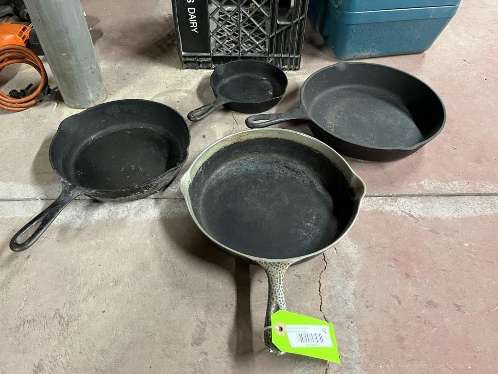 Four cast iron skillets of varying sizes on a concrete floor.