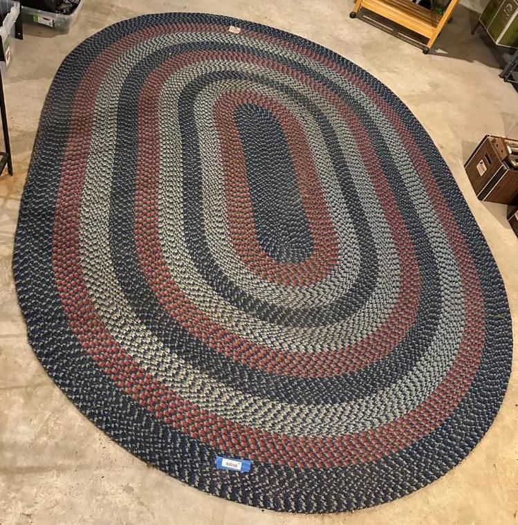 Oval braided rug in navy, red, and gray on a concrete floor.