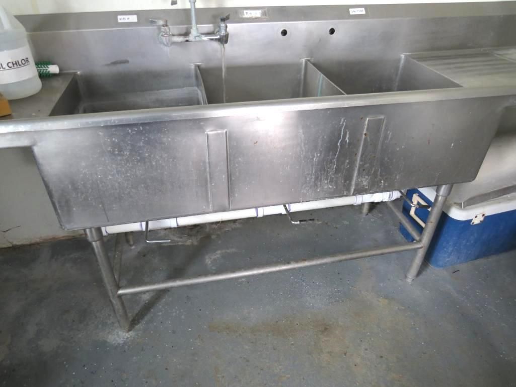 Stainless steel three-basin sink in a commercial kitchen setting, with a faucet running water.