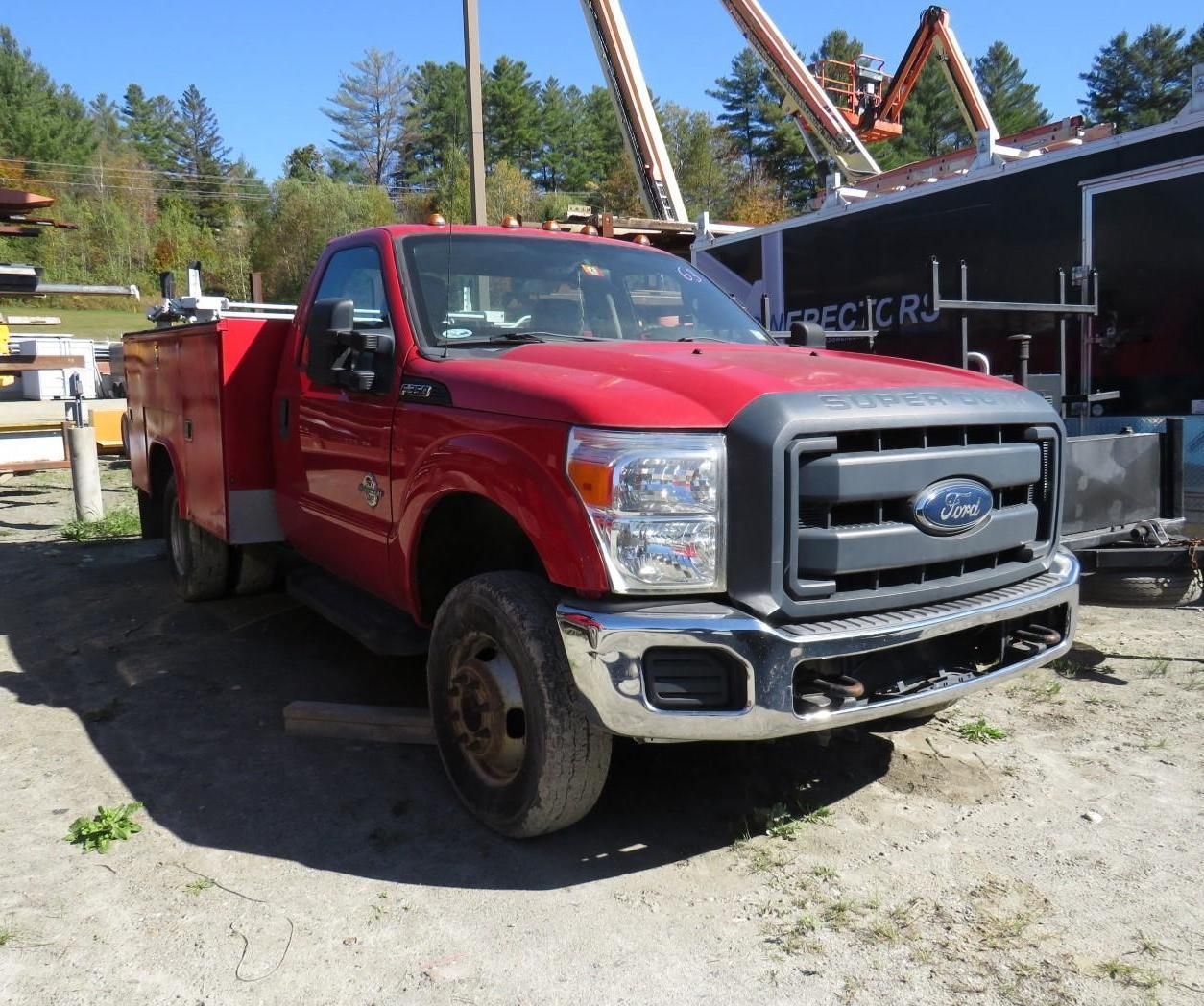 Red Ford F-350 dually truck parked on dirt in a construction area, with a black front grill and a utility bed.