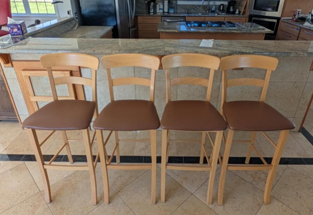Four wooden bar stools with brown seats lined up in front of a kitchen island.