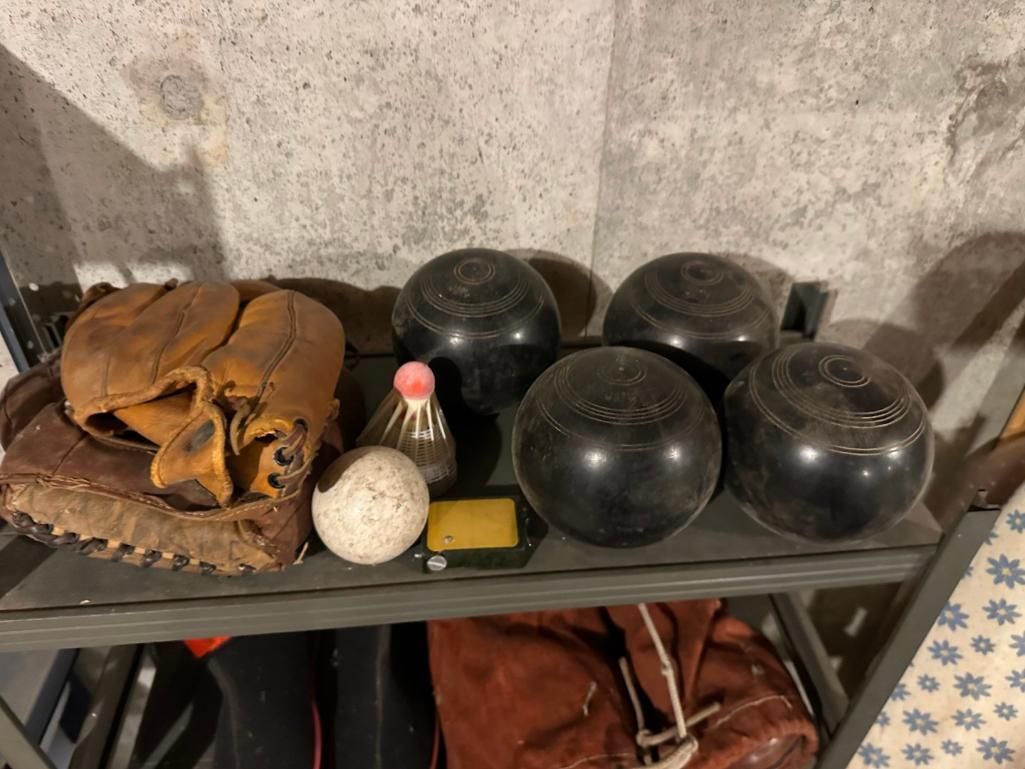 Shelf with black bocce balls, a glove, a white ball, and other items.