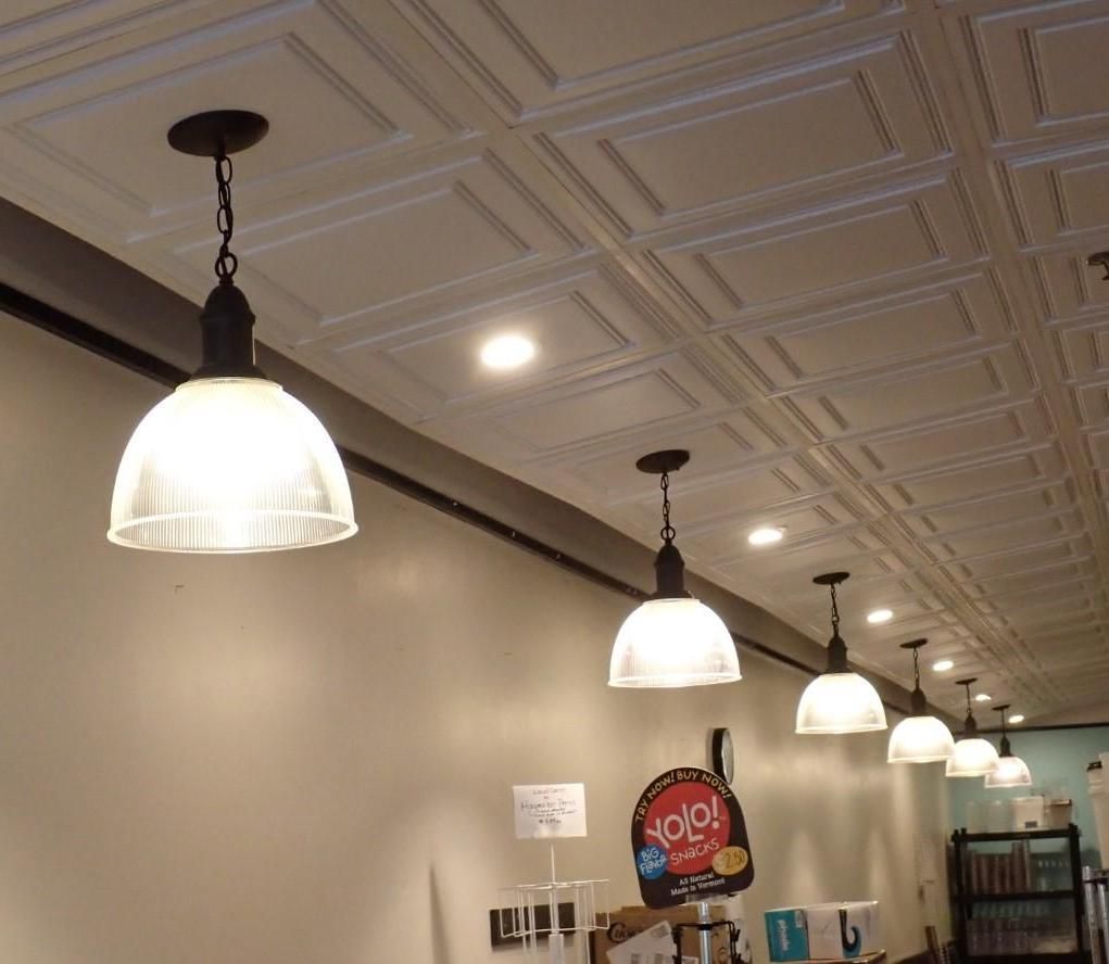 White ceiling tiles with hanging pendant lights over a counter with products and a sign.